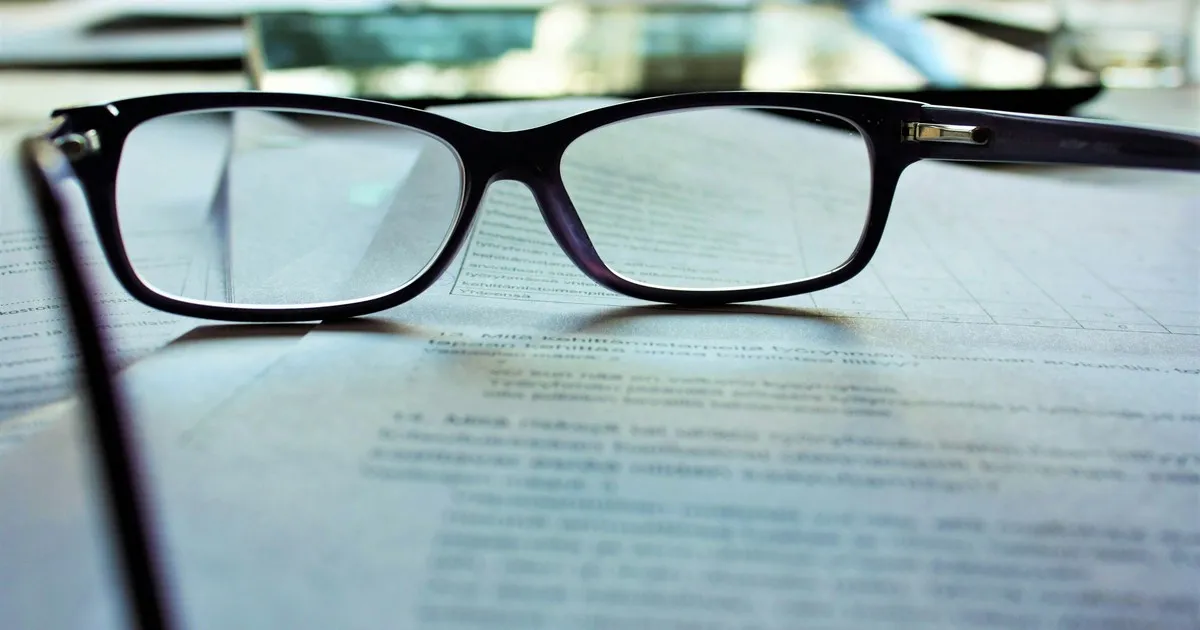 A pair of reading glasses resting on a printed page, the text soft-focused underneath