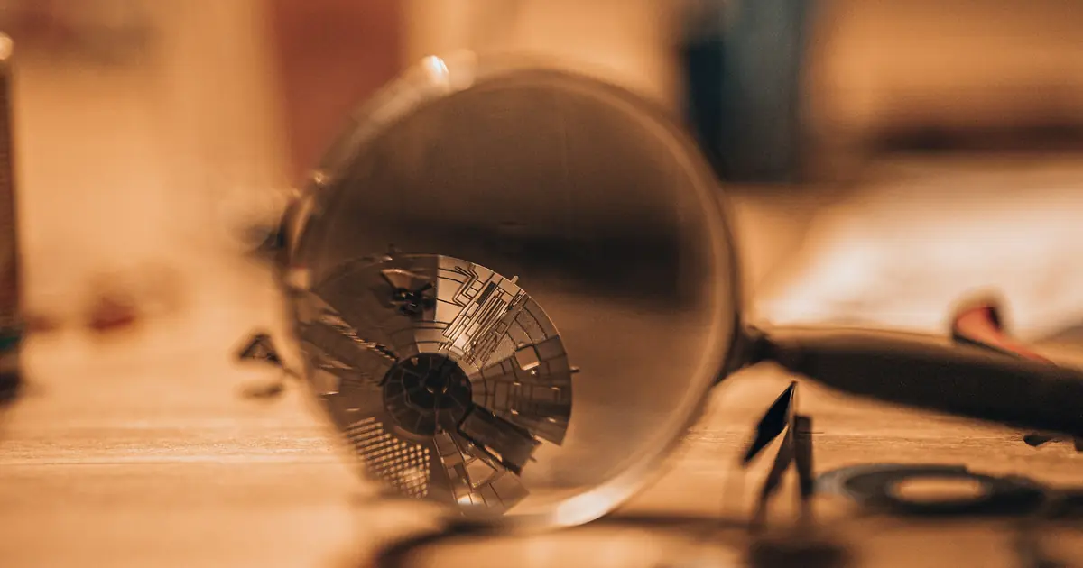A magnifying glass on a wooden workbench, reflecting a small mechanical part