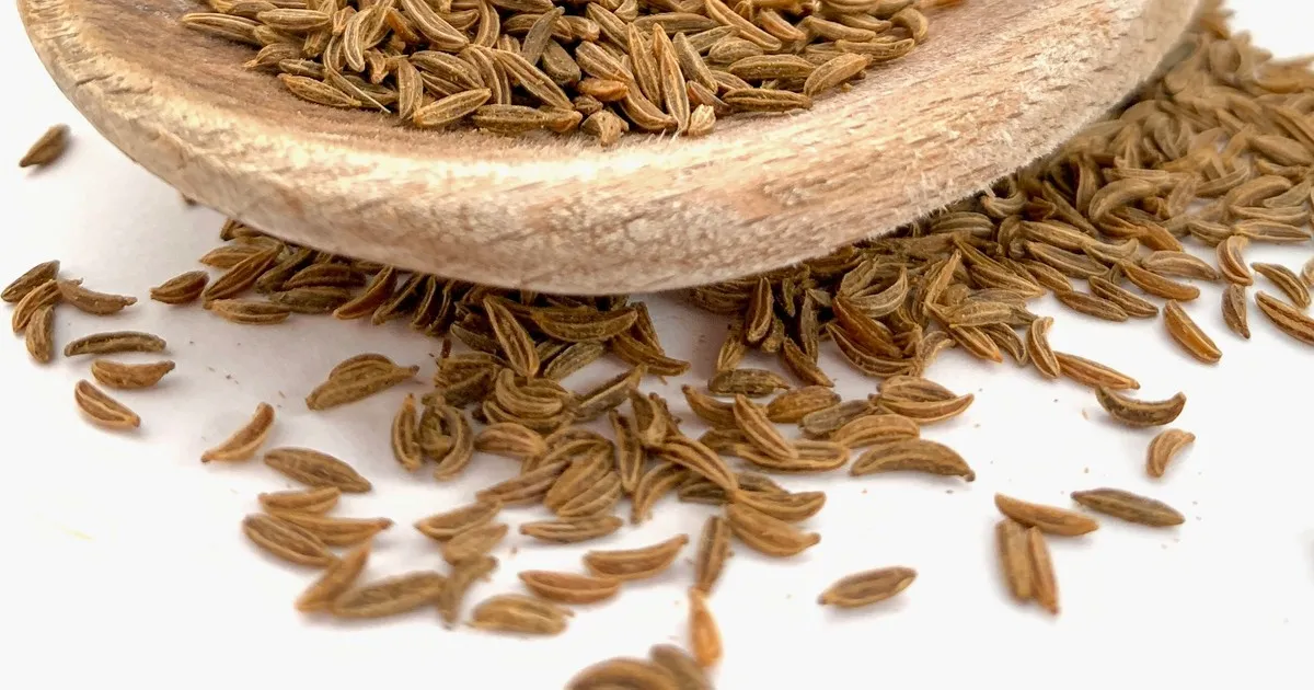 Small brown seeds spilling from a wooden spoon onto a white counter