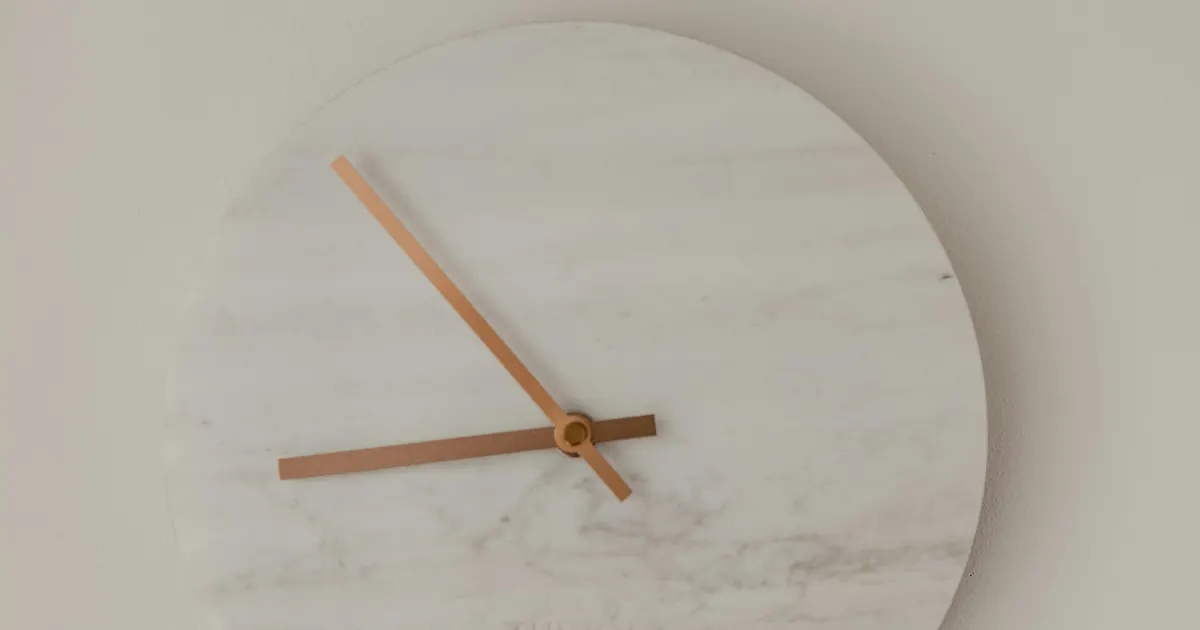 A round marble wall clock with copper hands, photographed at an angle