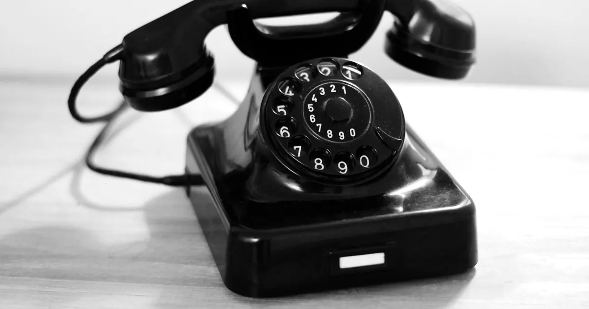 A black rotary telephone on a wooden table, in black and white