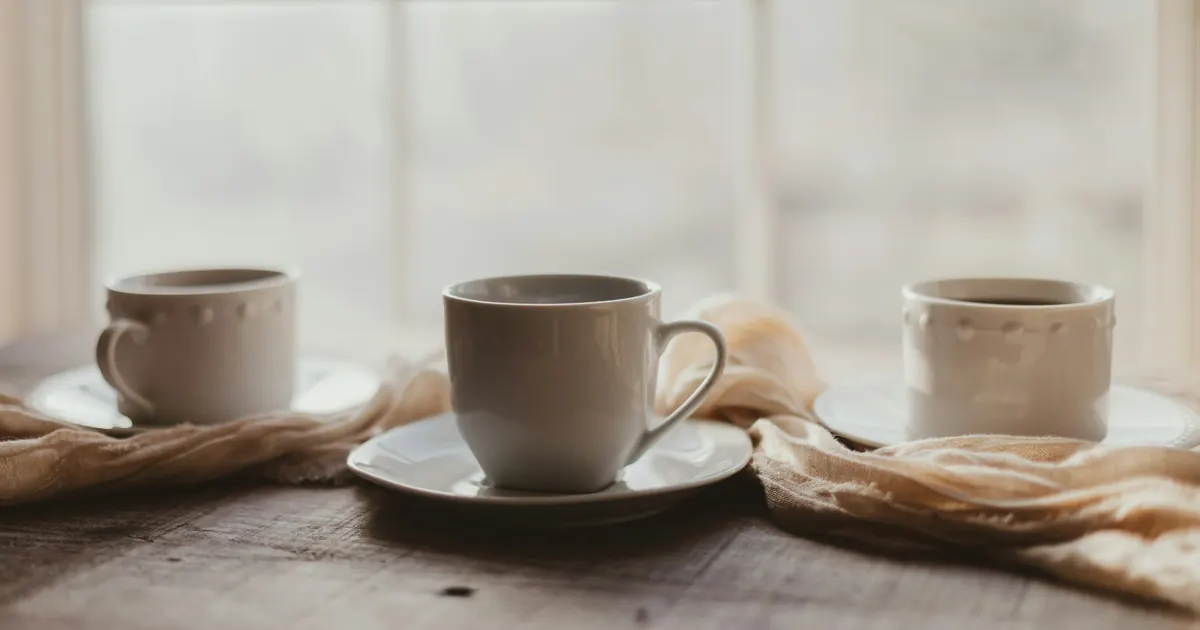 Three ceramic teacups set separately along a wooden table near a window