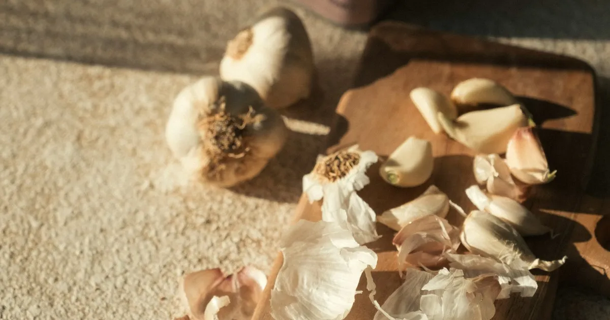 Garlic bulbs and peeled cloves scattered on a wooden cutting board in morning light