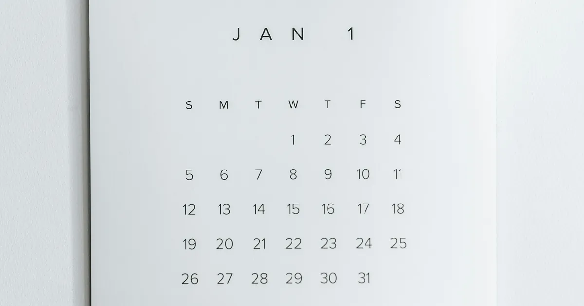 A close-up of a minimal paper wall calendar showing a grid of dates