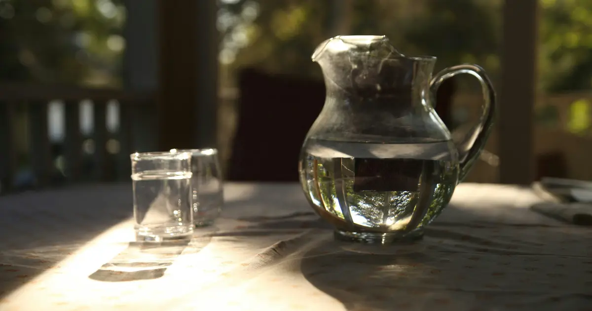 A glass water pitcher and two glasses on a table in warm morning light
