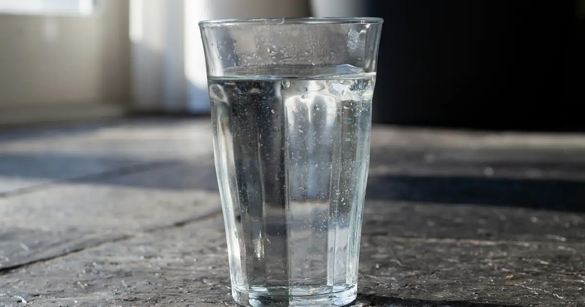A glass of water on a dark wooden table with soft morning light from a window