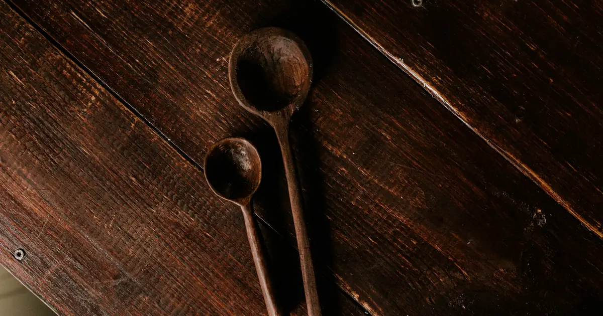 Two old wooden spoons of different sizes resting on a dark wood table