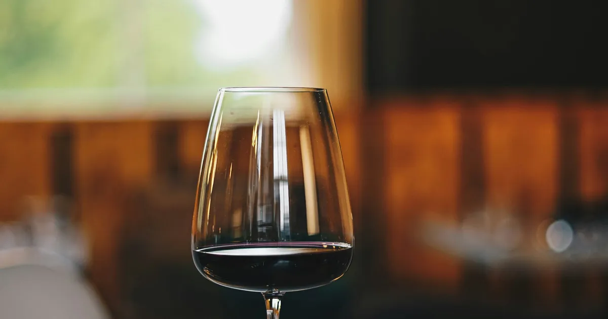 A glass of red wine on a table, backlit by soft window light