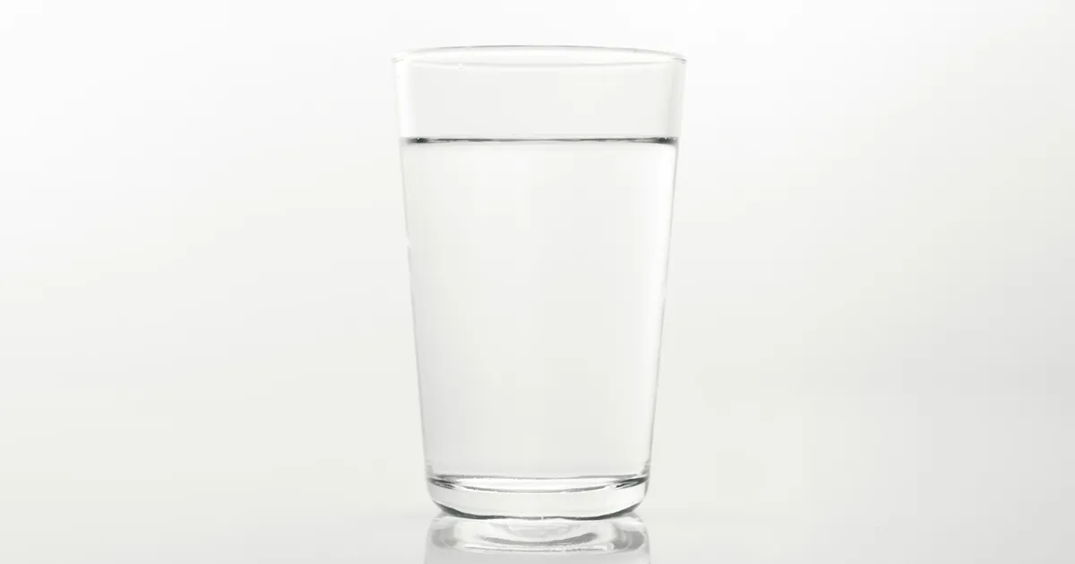 A glass of water on a plain white surface, backlit